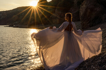A mysterious female silhouette with long braids stands on the sea beach with mountain views, Sunset...