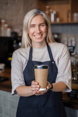 Shot of aged female barman working in coffee shop with blond hairs and coffee cup.