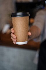 Shot of female barman holding brown and plastic coffee cup.
