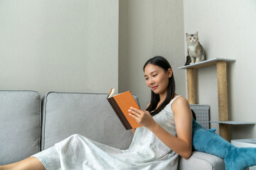 Young beautiful Asian woman relaxing on couch in apartment living room and reading a book in the...