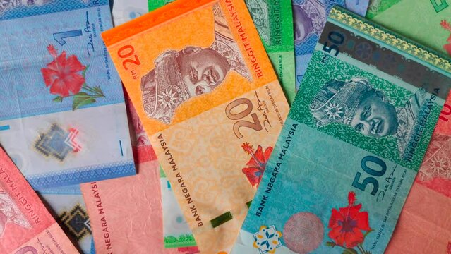 Rotating stack of Malaysian ringgit banknotes as background.