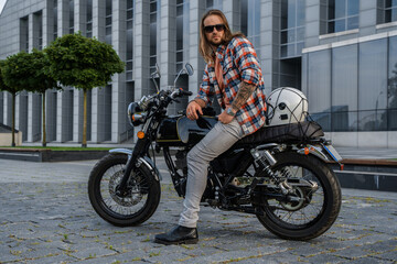 Fototapeta na wymiar Shot of trendy guy with long hairs driving motorcycle outdoors in daytime.