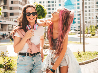 Two young beautiful smiling hipster female in trendy summer clothes.Sexy carefree women posing in the street with pink hair. Positive pure models having fun at sunset. Cheerful and happy