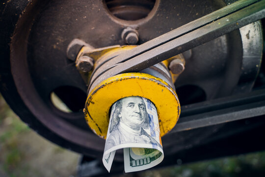 A rolled one hundred dollar bill close-up in a tractor engine pulley. Funding for agricultural land. The cost of maintenance and production on the farm. Purchase and repair of agricultural machinery