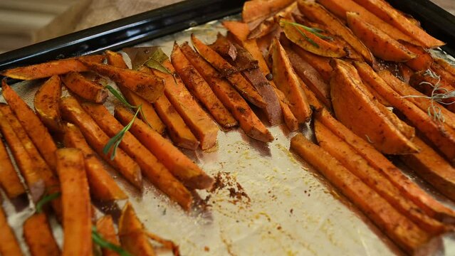 Healthy homemade sweet potato fries on a baking sheet. Delicious vegan meal - roasted batata wedges baked with rosemary leaves. Close-up. Delicious healthy vegan meal.