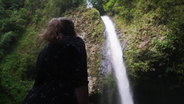 Low angle shot of a women standing in front of a huge waterfall and beeing impressed by the nature creation