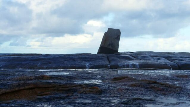 As the waves crash into the underrock sea cave water surges from the granite blowhole