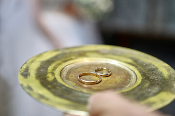 During a church wedding, gold wedding rings are held on a tray in the hands.