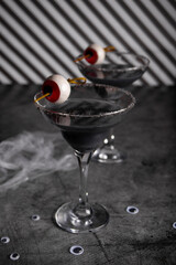 Halloween black cocktail in glasses with candy eyeball. Party festive celebrate concept.