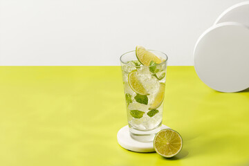 Mojito, Iced cold summer cocktail drink on podium. Glass of cold tonic with lime. Lemonade with ice and mint on green background.
