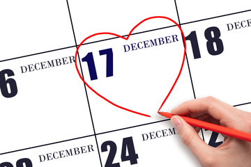 A woman's hand drawing a red heart shape on the calendar date of 17 December. Heart as a symbol of...