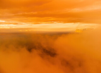A red burning sunset over the sea with rocky volcanic cliff. Abstract nature summer or spring ocean sea background. Small waves on golden warm water surface with bokeh lights from sun.
