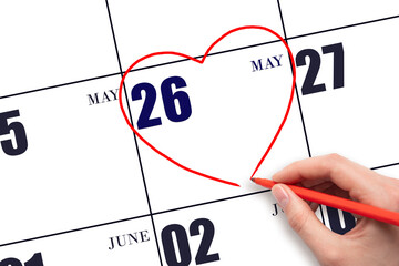 A woman's hand drawing a red heart shape on the calendar date of 26 May. Heart as a symbol of love.