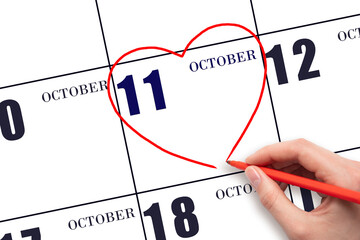 A woman's hand drawing a red heart shape on the calendar date of 11 October. Heart as a symbol of love.