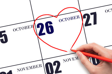 A woman's hand drawing a red heart shape on the calendar date of 26 October. Heart as a symbol of love.