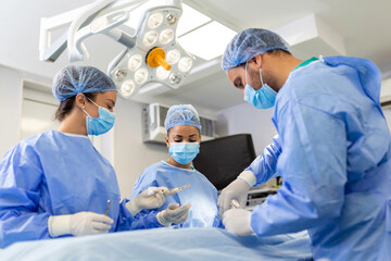 Medical team performing operation. Group of surgeon at work in operating theatre toned in blue. Doctor operation in operation room at hospital concept for insurance advertising.