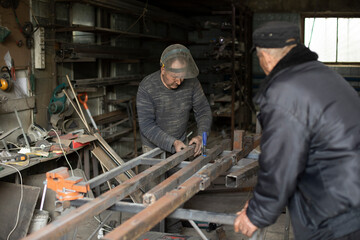 Welder holds metal. People in metal workshop. Work in garage.