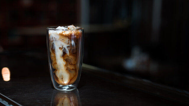 Ice coffee on a table with cream being poured into it showing the texture