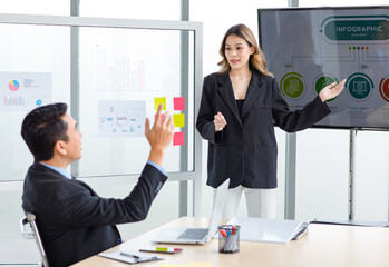 Millennial Asian successful professional female businesswoman presenter speaker in formal suit standing explaining answering unrecognizable male businessman rise hand asking question in meeting room