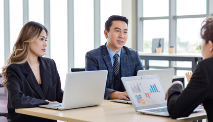 Millennial Asian successful professional male businessman female businesswoman in formal suit sitting together at working desk with laptop computer talking sharing business ideas in company office