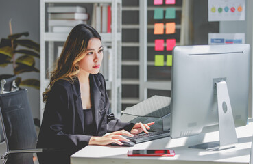 Millennial Asian cheerful successful professional female businesswoman sitting smiling using typing...