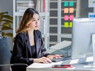 Millennial Asian cheerful successful professional female businesswoman sitting smiling using typing...