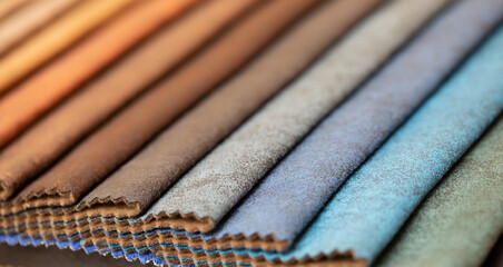 Fabric swatches in different colors are stacked for selection. A variety of shades of upholstery material for furniture and interior. Fabric texture close up. A set of multi-colored rolls of material.