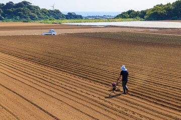 夏の終りに小さな耕運機で広い畑を耕す農夫