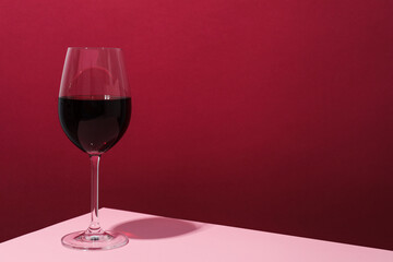 Glass of wine on pink table against crimson background, space for text