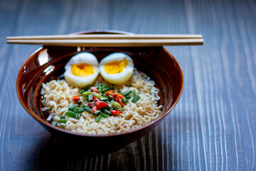 Today's dinner, hot noodles with soft-boiled eggs, sprinkled vegetables and pepper on a black wooden table.