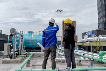 At construction site manager visit engineer working on the rooftop near pipe rack to inspection the progress by drone fly and  from the blue print drawing and look around and pointing and check hand
