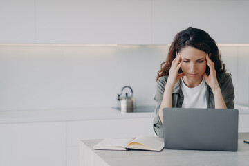Female suffers migraine headache during laptop work, solves working problem at home. Stress, burnout