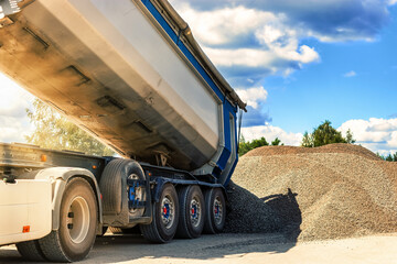 A large dump truck unloads rubble or gravel at a construction site. Car tonar for transportation of heavy bulk cargo. Providing the construction site with materials.