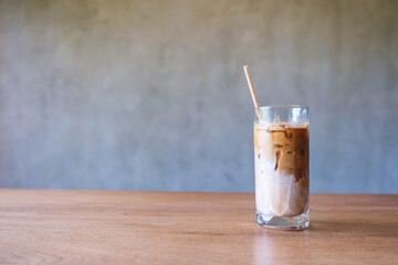 A glass of iced latte coffee with a bio straw on wooden table