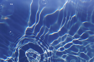 Bluewater waves on the surface ripples blurred. Defocus blurred transparent blue colored clear calm water surface texture with splash and bubbles. Water waves with shining pattern texture background.
