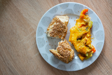 Bread with sesame seeds and scrambled eggs with peppers, tomatoes and mushrooms in a plate on a wooden table