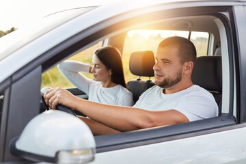 Young couple in sitting in a new car, man driving a automobile with his girlfriend and having fun, buying or renting an auto. Travel, tourism, recreation.