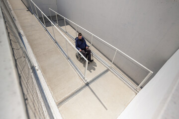 Man on electric wheelchair moving along concrete accessibility pathway near the building. Concept...