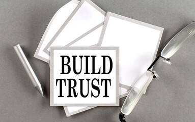BUILD TRUST text written on a sticky with pencil and glasses