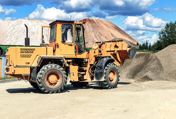 A large front loader transports crushed stone or gravel in a bucket at a construction site or concrete plant. Transportation of bulk materials. Construction equipment. Bulk cargo transportation.