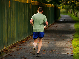 One man in green t shirt and blue shorts running in a park. Sport activity. People jogging. Healthy lifestyle concept.