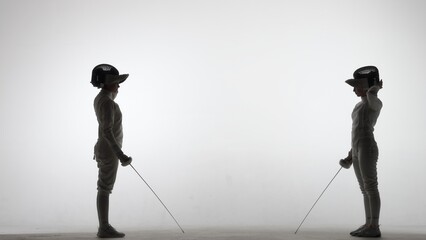 Side view of two young female swordswoman with rapiers. Athletes in uniforms and protective helmet...
