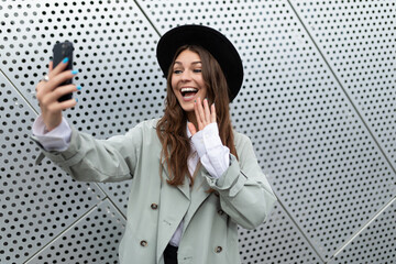 young woman emotionally talking on a video link of a mobile phone against the background of an aluminum facade of an office building