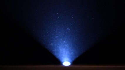 Small particles of dust illuminated by a blue beam of light on a black studio background. Powder or...