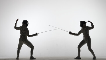 Side view of two young female swordswoman with crossed rapiers. Athletes in uniforms and protective...