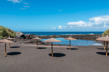 Scenic sea view on beach Playa Charco del Conde without people in Valle Gran Rey, La Gomera, Canary Islands, Spain, Europe. Straw umbrellas in the dark volcanic sand. Vacation vibes in tropical bay
