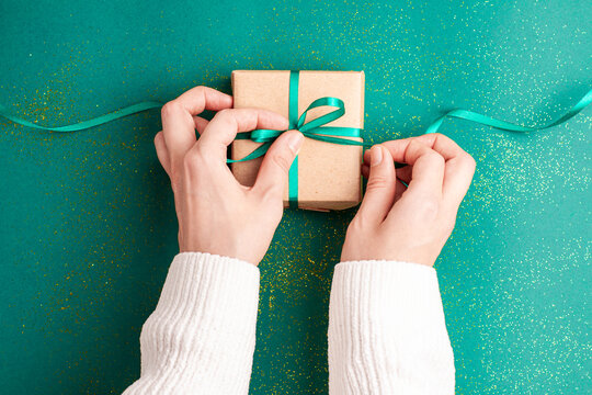 Human Hands In White Sweater Untied Brown Gift Box With A Emerald Green Satin Ribbon Bow On Green Background With Gold Colored Glitter Christmas Holidays Concept Flat Lay