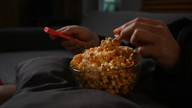 Close up view man hand grabbing popcorn and watching television at night. Leisure activity, relaxation, hobby concept