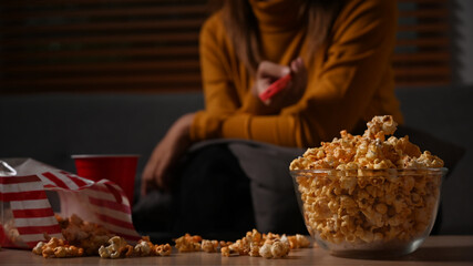 Bowl of popcorn and cup on wooden table with young woman sitting in background. Entertainment and leisure activity concept