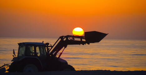 A tractor at sunset with the sun in its shovel, symbolizing energy supply